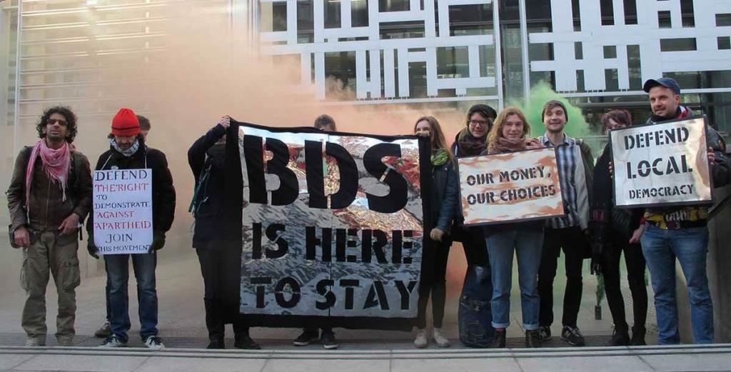 Campaigners hold placards and banners that read: "Defend the right to demonstrate against apartheid – Join this movement"; "BDS is here to stay"; Our money, our choices"; "Defend Local Democracy". Credit: London Palestine Action