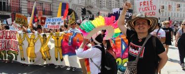 War on Want's Senior Programme's Officer Seb Munoz raises a fist at the front of a colourful Latin American contingent at a rally.