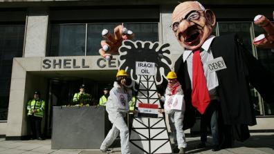 Hands Off Iraqi Oil demo, 2008. Activists dressed as oil industry workers are outside of a Shell building, with a model of an oil drilling rig labelled "Iraqi oil", in front of a large caricature model labelled "Chaney".